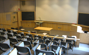 Tiered lecture hall with projector screen and blackboards at the front of the room.