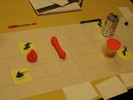 A grid on white paper contains a Diet Coke can, a Play-Doh tub, a large blob and a sausage of pink Play-Doh scattered about.
