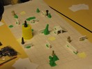 Mid-game, the board contains several structures of dominos, hills and lakes of green Play-Doh, and chess pieces with Play-Doh arms or faces. One rook is standing on its head.