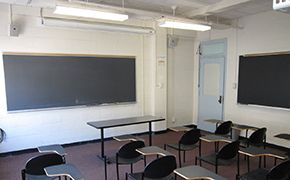 Three rows of tablet armchairs facing a black chalkboard. There is a classroom door on the right wall.