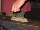A rectangular chunk of grey clay is smashed at one end by hand, to demonstrate how hammer blows deform hot metal.
