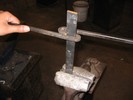 A metal bar is clamped in a vise, and tucked into one curve of the S, which twists it as the long handles are turned around.