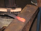 Coarse wire bristles scrub the surface of a red-hot workpiece.