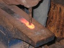 A round 1/4-inch punch is applied to a yellow-hot workpiece.