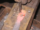 Zooming in, the red-hot metal is nearly cut through, so a bronze plate is placed under the workpiece with a hold-down.