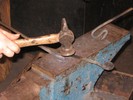 The twisted bar lies on the anvil face as a loop is made in one end of another bar.