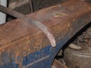 A twisted 1/2-inch square bar begins to be bent over the corner of the anvil face. Flattened corners show where the hammer has fallen.