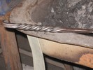Two round and two square bars are forge welded together, twisted around each other, and scrolled at the end.
