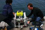 Two students lifting the ROV at the dock's edge.