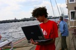 Student on a boat dock, holding a laptop computer.