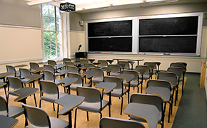 A classroom that can accommodate 42 students. It has several small student desks, four blackboards, and a projector.