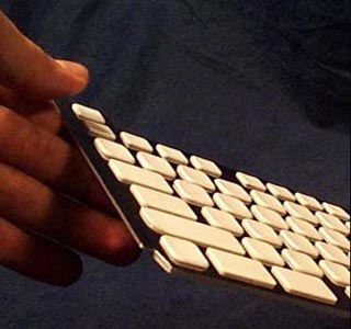 A photo of a hand holding a corner of a keyboard.