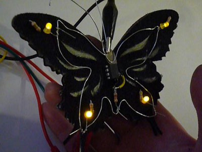Photo of the PCButterfly in dim background light, with LEDs lit up. 