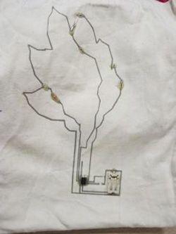 A photo showing the outline of the tree in lasercut fabric, and another photo of the tree with components and spots of epoxy added. 