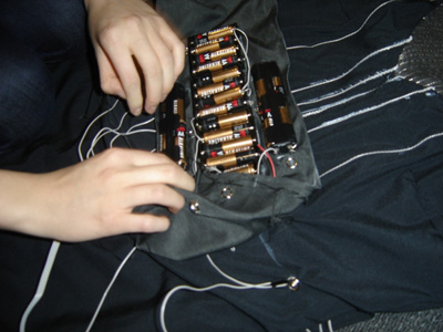 Photo close-up of a rectangular fabric pouch on the dress, containing many AA batteries.
