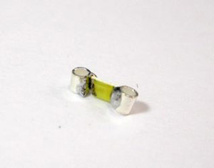Photo of a small piece yellow plastic with two small silver cylinders on either end.