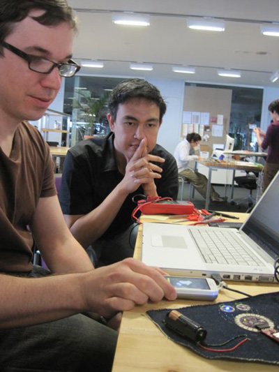 Photo of two people at a table working on the system: mobile phone, wristband, and laptop.