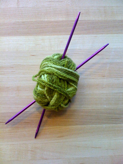 Photo of a ball of yarn with two knitting needles.
