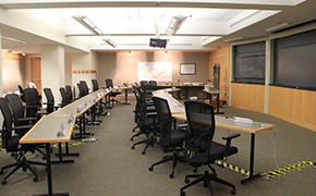 Ten grey rectangular tables arranged in two rows facing sliding blackboards. LCD projector mounted to ceiling in center of room.