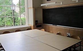 A classroom with chalkboards and a large square table with chairs around it.