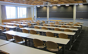 A classroom with chalkboards, several rows of flat tables for students, and a small table at the front for the instructors.