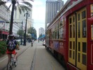 A streetcar drives down a city street. A bicyclist rides next to it.