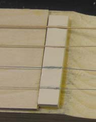 Four guitar strings stretched over neck nut blank.