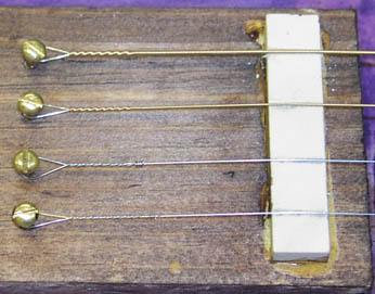 Four guitar strings stretched over tailpiece nut blank.