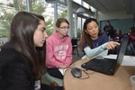 Girls sit around a laptop, and a volunteer is pointing to the computer screen.
