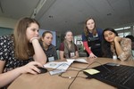 Girls sit around a laptop, one of them is using the mouse. A volunteer looks over her shoulder.